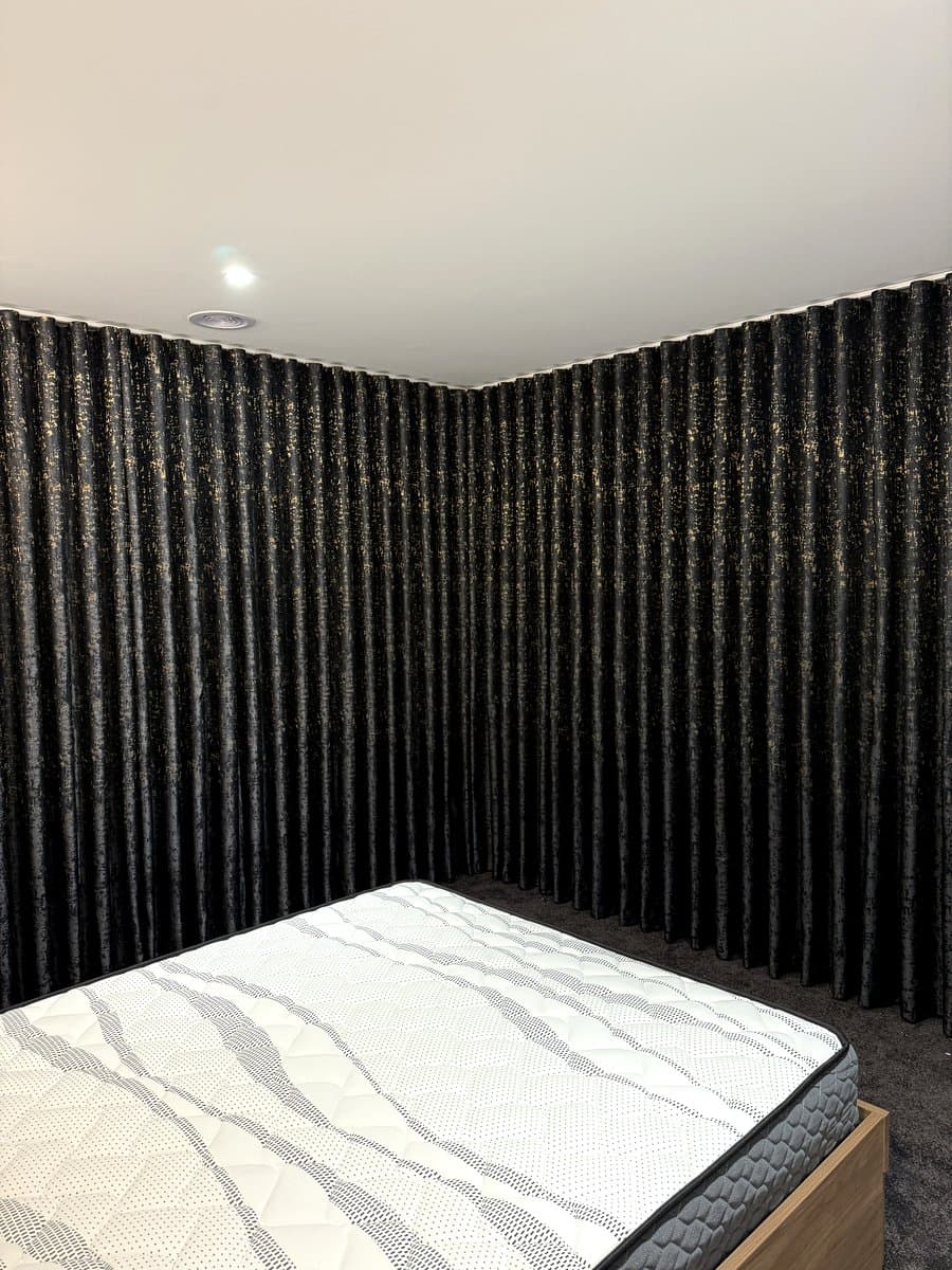 Black and gold blockout curtains on a curved corner window in a bedroom